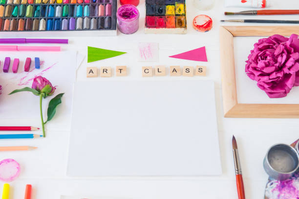 istock Top view creative artist workplace. Blank Canvas, Art class lettering on wooden blocks and various colorful painting materials and flowers on white background.Art therapy, Drawing lessons. Flat lay. 1151353362
