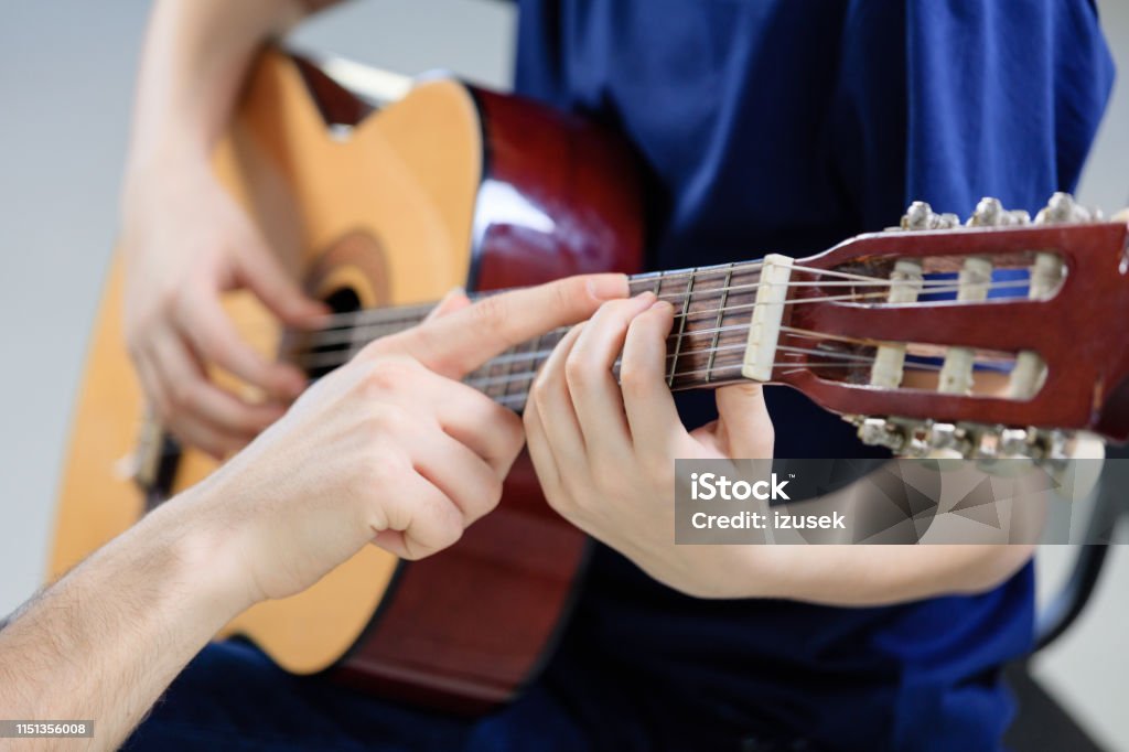 Trainer explaining guitar strings to student Cropped image of teacher explaining guitar strings to student on fretboard. Pre-adolescent boy is learning musical instrument in class. They are playing music at conservatory. Conservatory - Education Building Stock Photo