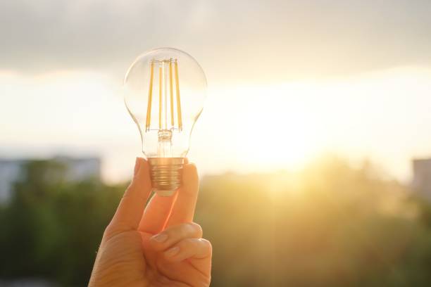 istock Filament led lightbulbs, hand holding lamp, evening sunset sky background 1151360667