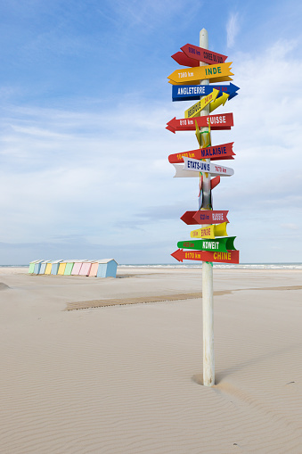 Signpost with directions to international locations at the beach of Berck-Plage, France. Colorful beach cabins in background.
