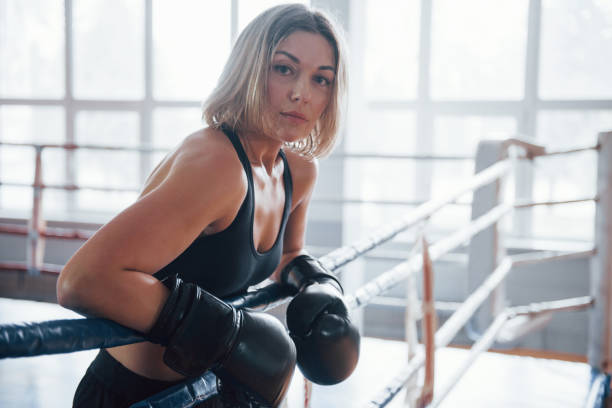 Looks to the camera. Female sportswoman in the boxing ring. In black colored clothes Looks to the camera. Female sportswoman in the boxing ring. In black colored clothes. women boxing sport exercising stock pictures, royalty-free photos & images
