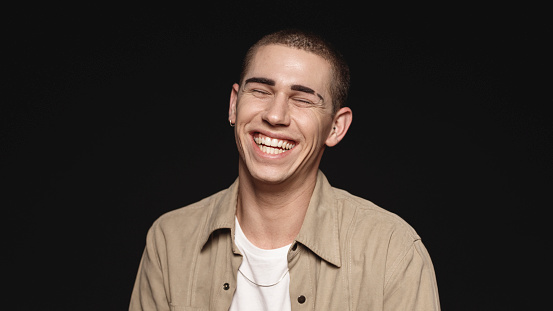 Portrait of a caucasian man laughing with closed eyes. Close up of a man laughing isolated on black background.