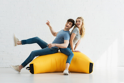 cheerful blonde girl and happy man sitting on yellow bean bag chair
