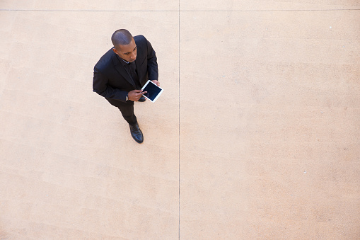 Successful businessman with tablet walking through office lobby. Top view of black man in formal suit using tablet and walking. Communication concept