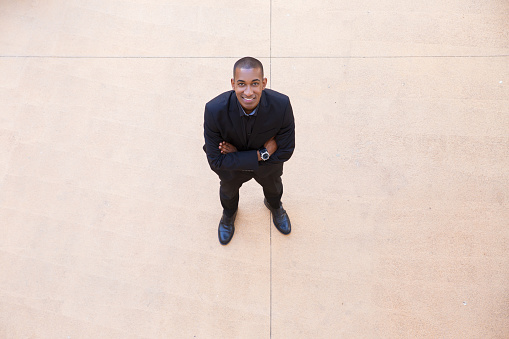 Happy confident businessman posing in office lobby. Top view of black man in formal suit crossing arms and smiling at camera. Confident businessman concept