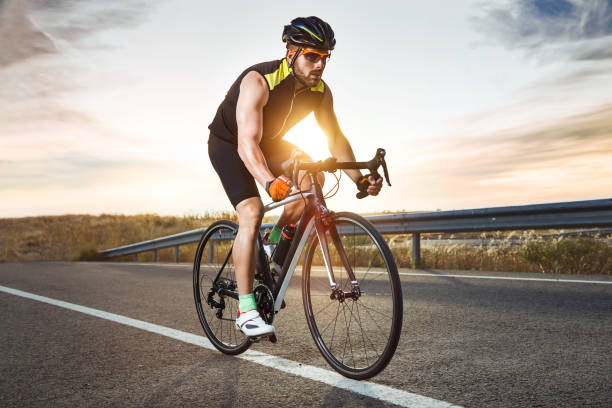 homem novo considerável que ciclagem na estrada. - roupa desportiva de protecção - fotografias e filmes do acervo