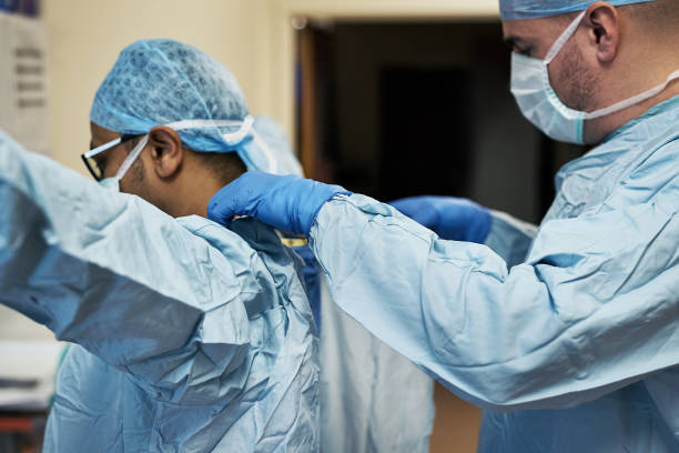 First rule of the operating room: Keep it clean Shot of two surgeons helping each other get dressed in preparation for a surgery putting on latex gloves stock pictures, royalty-free photos & images
