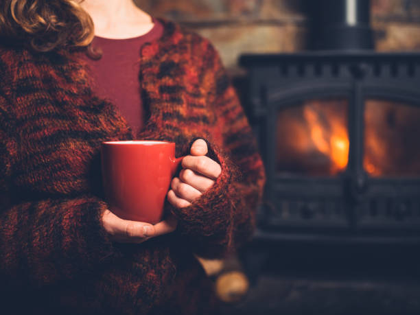 istock Woman in red jumper with mug by fire 1151376736