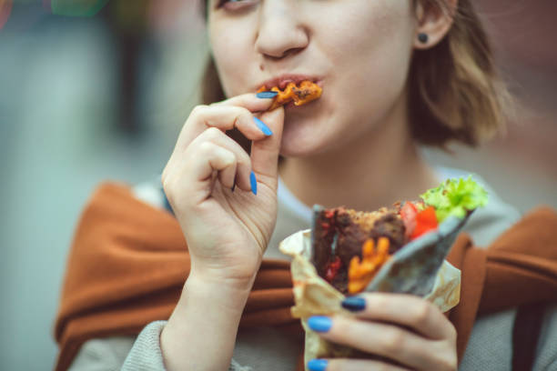 szczęśliwa młoda dziewczyna ciesząc się jedzeniem ulicznym w mieście w lecie - female mobility blank teenage girls zdjęcia i obrazy z banku zdjęć
