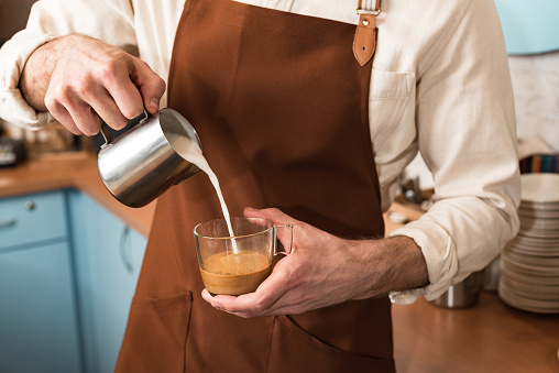 Cropped view of barista pouring milk in coffee