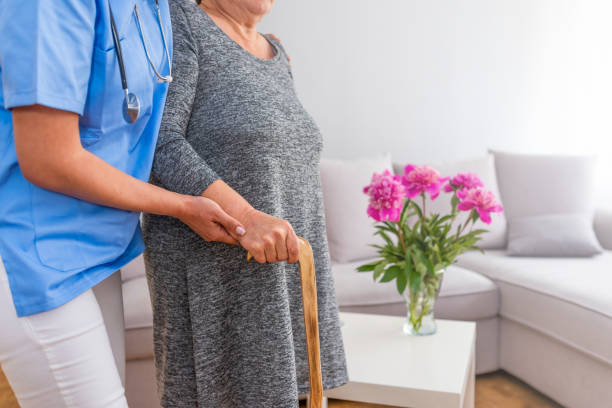 Concept senior people health care. Senior Woman's Hands On Walking Stick With Care Worker In Background. Senior woman with her caregiver at home. Concept senior people health care. walking aide stock pictures, royalty-free photos & images