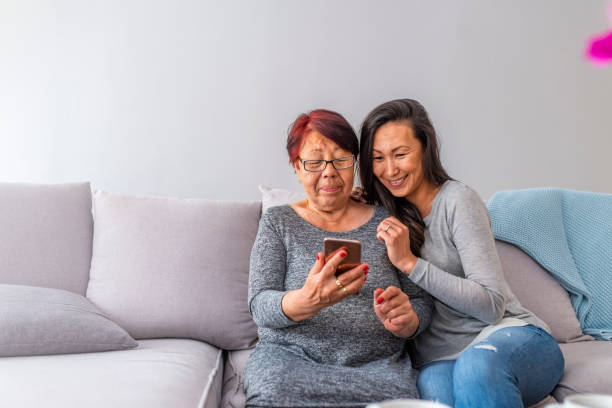 happy asian woman and her mother with smartphone at home - wireless technology cheerful granddaughter grandmother imagens e fotografias de stock