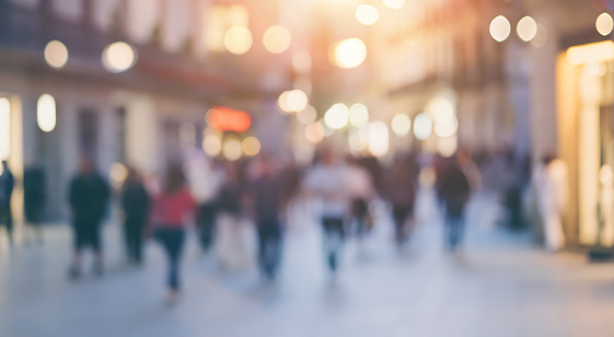 Group of unrecognizable anonymous people in bokeh walking on a street in the evening. Blurred image