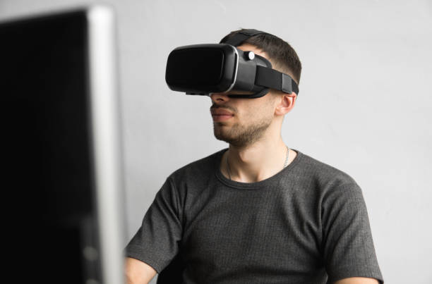 istock Young man wearing virtual reality goggles headset, vr box and sitting in the office against computer monitor. Connection, technology, new generation, progress concept. 1151402885
