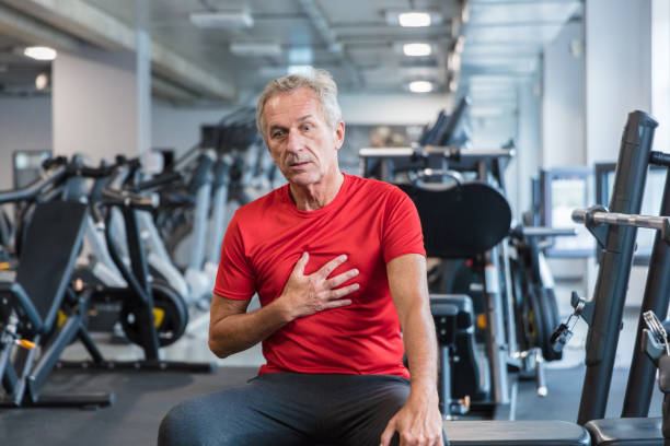 Elderly man feeling chest pain at gym Shot of a elderly man feeling chest pain at gym. Senior man feeling tired after workout at rehab centre. male chest pain stock pictures, royalty-free photos & images