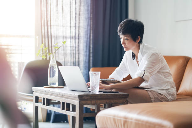 donna asiatica freelance digitando su laptop mentre lavora a casa - laptop adult curtain business foto e immagini stock