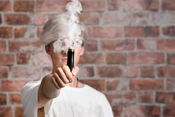 Vaper Smoke outdoor electronic cigarette near the brick wall. Young man smoking big cloud of steam stock photo