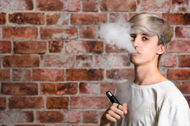 Vaper Smoke outdoor electronic cigarette near the brick wall. Young man smoking big cloud of steam stock photo