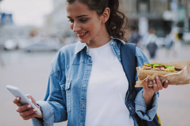 istock Pretty female checking mobile with hot dog in hand 1151411418