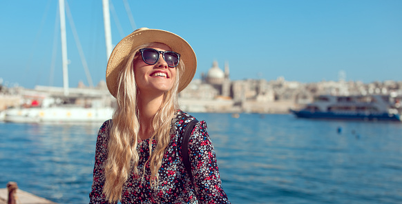 Happy blonde tourist lady in hat enjoying mediterranean city at sea and sunshine