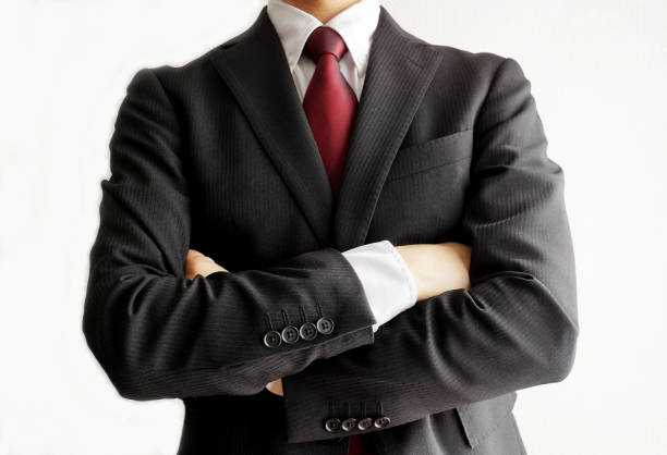 Full body of surprised young male employee with dark hair in elegant suit standing against white background with crossed arms and looking away with doubt