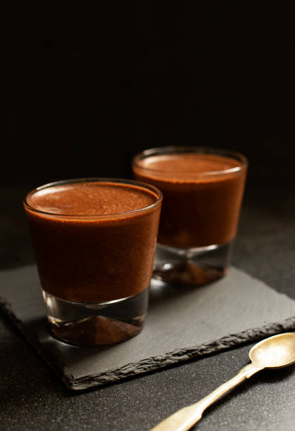 istock Chocolate pudding, souffle or mousse in glasses on a black stone plate on a black background, with a vintage copper spoon. Close-up. Space for text. Vertical. Selective focus 1151414004