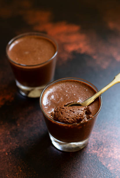 istock Chocolate pudding, souffle or mousse in glasses on a dark vintage background, with a vintage copper spoon. Spoon with dessert. Close-up. Space for text. Vertical. Selective focus 1151414207
