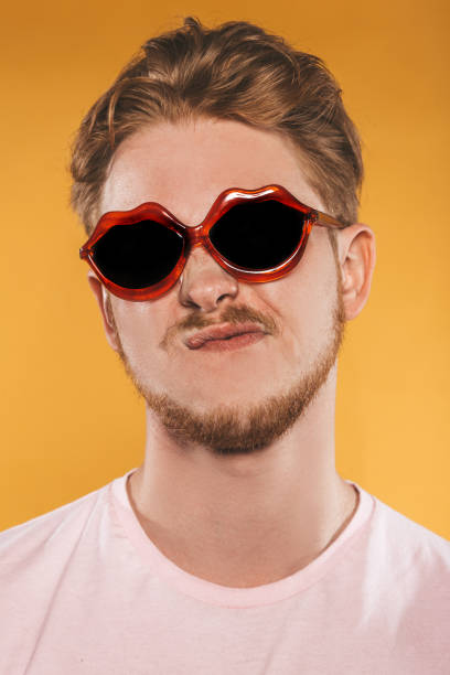 istock Grimacing young man in lip shaped sunglasses on yellow background 1151417359