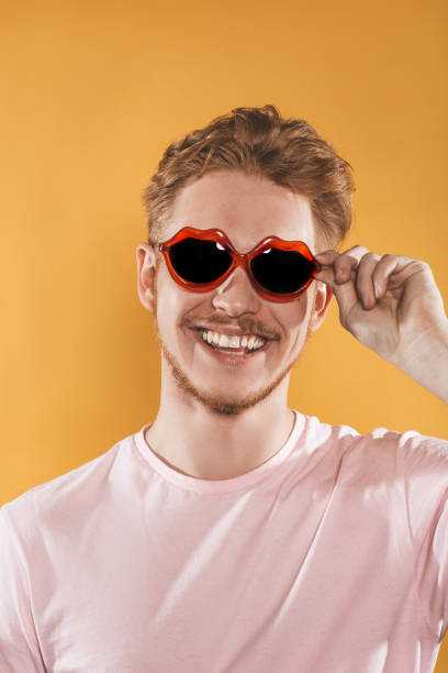 istock Laughing young man in lip shaped sunglasses on yellow background 1151417397