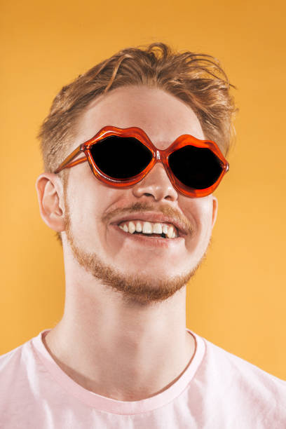 istock Laughing young man in lip shaped sunglasses on yellow background 1151417425