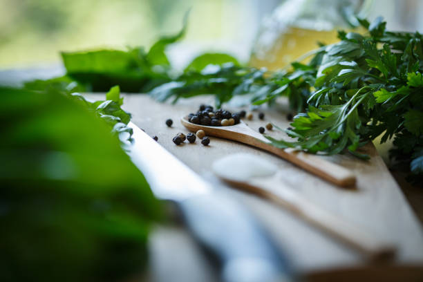 Close up shot of wooden spoons with salt and pepper lying on a cutting board surrounded with fresh herbs. Parsley, basil and chard.