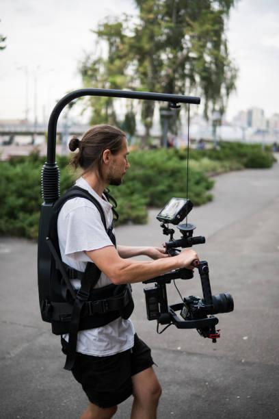 istock Professional videographer holding camera on 3-axis gimbal which mounted on easy rig. Videographer using steadicam. Pro equipment helps to make high quality video without shaking. 1151422522