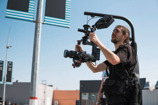 istock Professional videographer holding camera on 3-axis gimbal which mounted on easy rig. Videographer using steadicam. Pro equipment helps to make high quality video without shaking. 1151423736