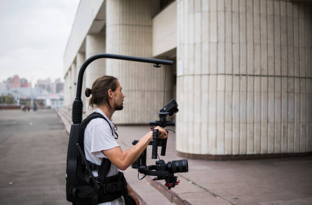 istock Professional videographer holding camera on 3-axis gimbal which mounted on easy rig. Videographer using steadicam. Pro equipment helps to make high quality video without shaking. 1151423894