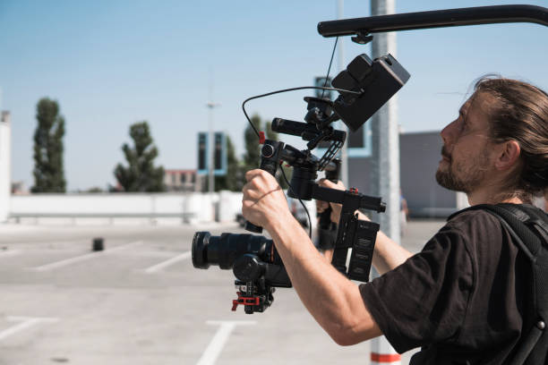 istock Professional videographer holding camera on 3-axis gimbal which mounted on easy rig. Videographer using steadicam. Pro equipment helps to make high quality video without shaking. 1151423958