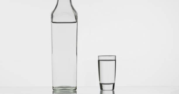 colpo di vodka in bicchiere e bottiglia. sfondo bianco - still shot foto e immagini stock