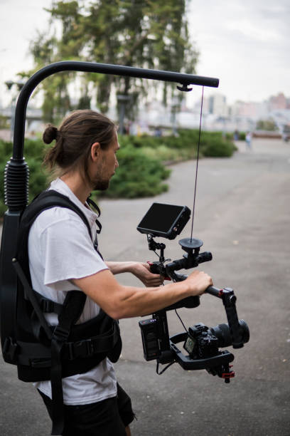 istock Professional videographer holding camera on 3-axis gimbal which mounted on easy rig. Videographer using steadicam. Pro equipment helps to make high quality video without shaking. 1151425396
