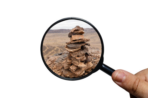 Stone pile mark on the mountain peak, view through a magnifying glass, white background, magnifying glass in hand