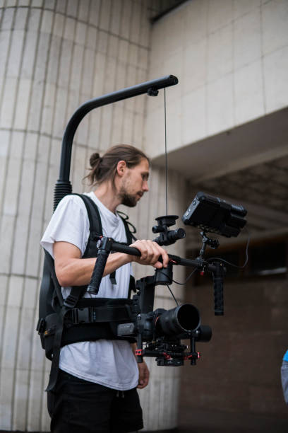 istock Professional videographer holding camera on 3-axis gimbal which mounted on easy rig. Videographer using steadicam. Pro equipment helps to make high quality video without shaking. 1151426556