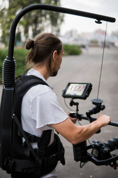 istock Professional videographer holding camera on 3-axis gimbal which mounted on easy rig. Videographer using steadicam. Pro equipment helps to make high quality video without shaking. 1151426719