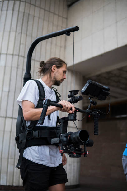 istock Professional videographer holding camera on 3-axis gimbal which mounted on easy rig. Videographer using steadicam. Pro equipment helps to make high quality video without shaking. 1151427087