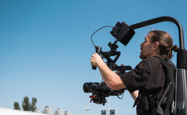 istock Professional videographer holding camera on 3-axis gimbal which mounted on easy rig. Videographer using steadicam. Pro equipment helps to make high quality video without shaking. 1151427999