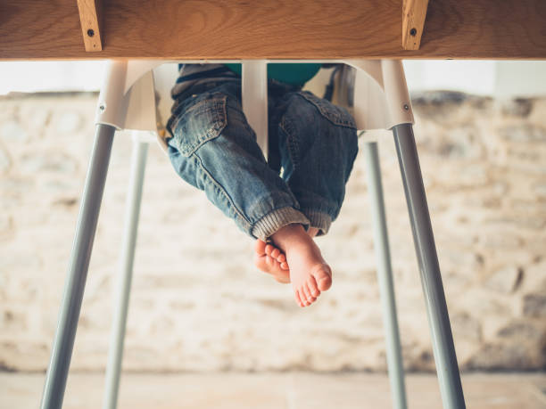 The legs of a toddler in a high chair at the table stock photo