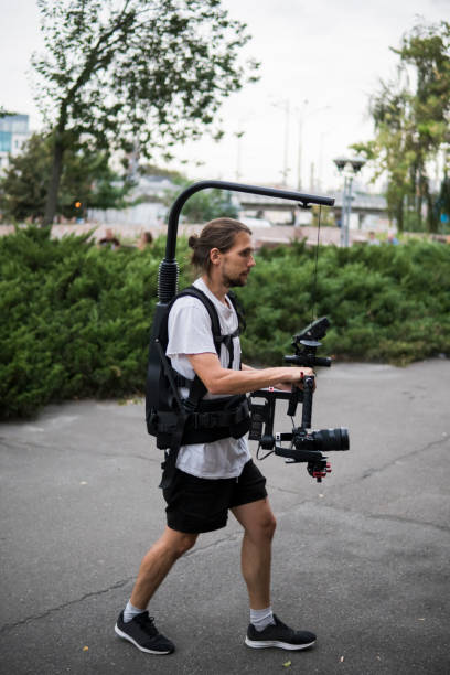 istock Professional videographer holding camera on 3-axis gimbal which mounted on easy rig. Videographer using steadicam. Pro equipment helps to make high quality video without shaking. 1151428176