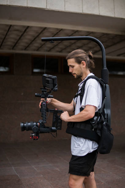 istock Professional videographer holding camera on 3-axis gimbal which mounted on easy rig. Videographer using steadicam. Pro equipment helps to make high quality video without shaking. 1151428243