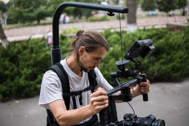 istock Professional videographer holding camera on 3-axis gimbal which mounted on easy rig. Videographer using steadicam. Pro equipment helps to make high quality video without shaking. 1151428432