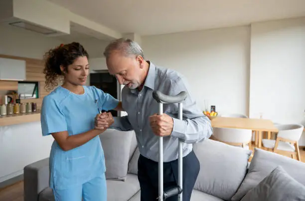 Latin American nurse helping a senior man in crutches at home - healthcare and medicine concepts