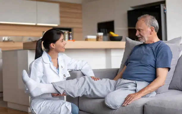 Doctor making visiting a disabled senior patient at home and checking his leg â assisted living concepts