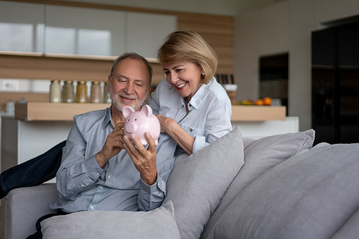 Portrait of a senior couple at home and holding their savings in a piggybank â home finances concepts