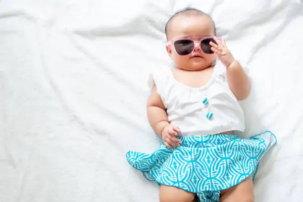 Photo of Asian baby girl wearing swimming suit and pink sunglasses on white background, baby in beach wear fashion